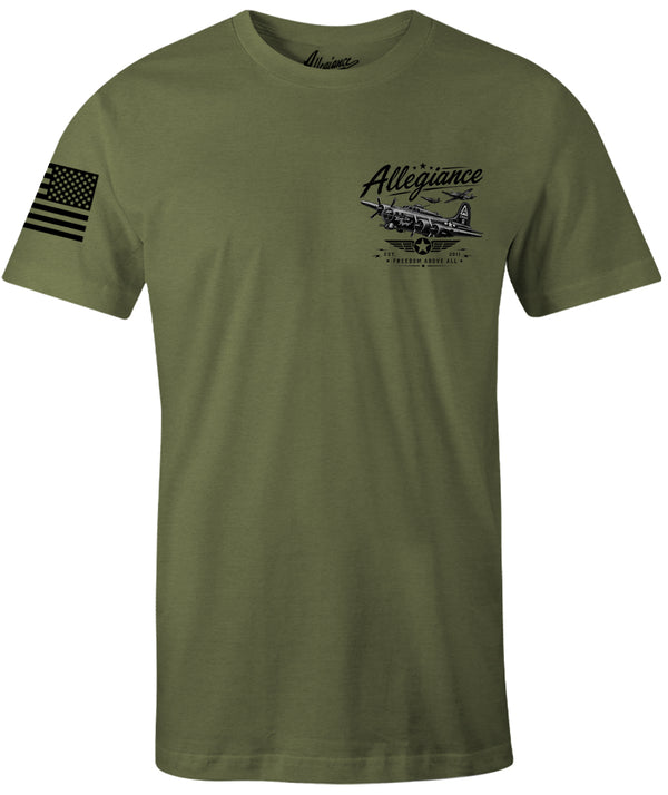 An olive green short-sleeve t-shirt with a black graphic on the left chest featuring a vintage airplane and the word 'Allegiance', plus a black American flag graphic on the right sleeve.